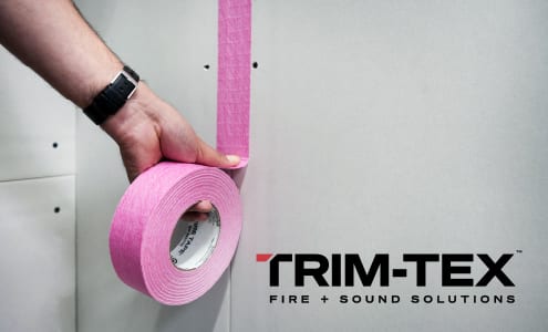 Hand applying pink Trim-Tex tape to a wall.