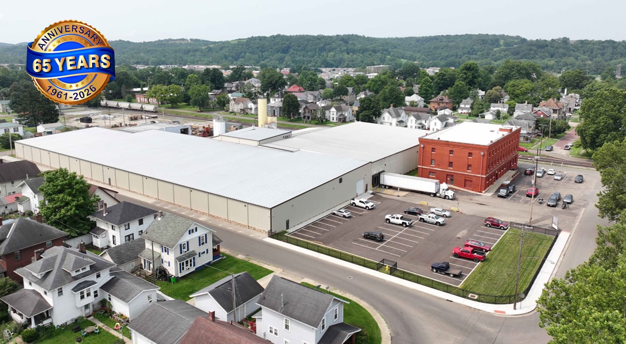 Aerial view: industrial building, residential area, hills. 65 years anniversary logo.
