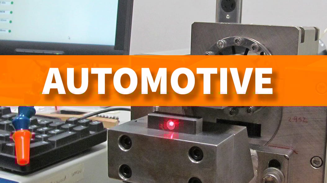 Lab equipment with a red laser dot, computer screen, and "AUTOMOTIVE" text overlaid.