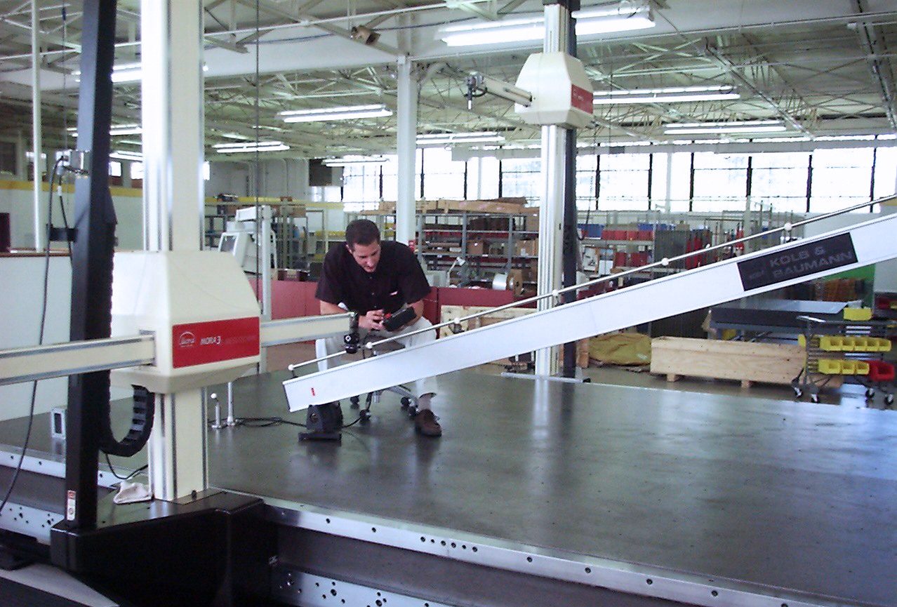 Man uses a large coordinate measuring machine in a bright factory.
