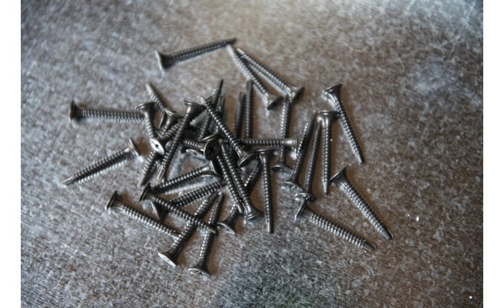 Pile of dark gray drywall screws scattered on a textured gray surface.