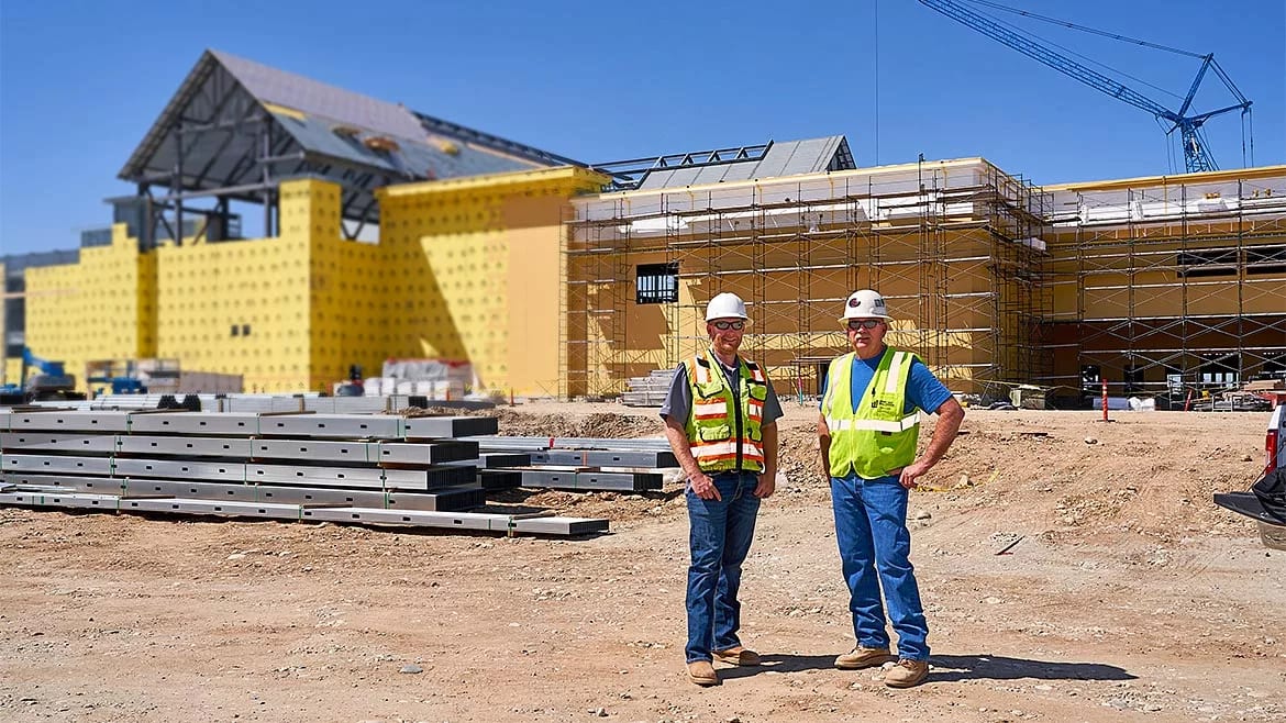 Two men in hard hats and safety vests at a building construction site.