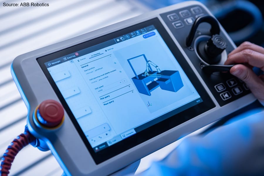 Hand operating an ABB Robotics controller displaying a robot arm simulation.