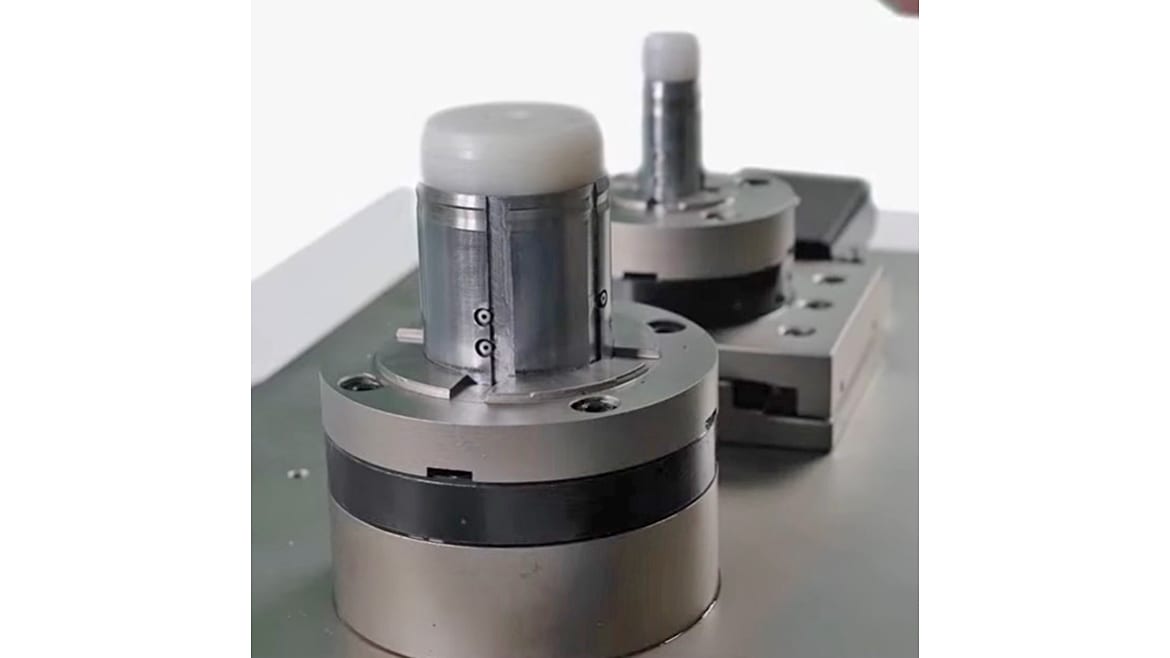 Close-up of two metallic industrial fixtures with white plastic caps, possibly chucks or testing equipment.