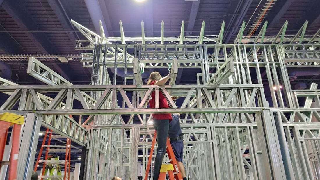 Person on a ladder working on assembling a complex metal frame structure for a building or display.