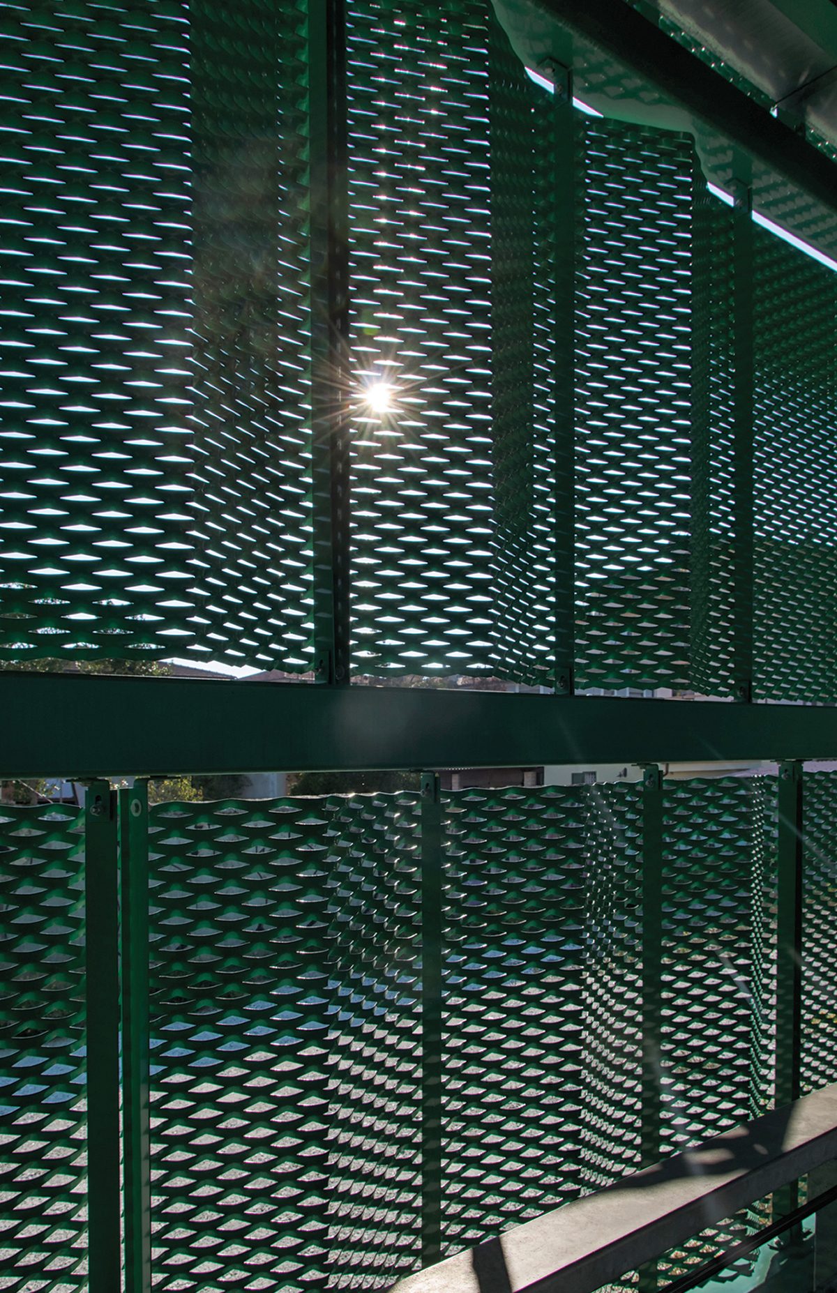 Sunlight bursts through layers of green expanded metal mesh, creating a vibrant pattern.