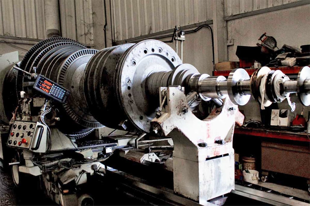A large industrial turbine rotor on a heavy-duty lathe with a digital readout, undergoing machining or balancing.