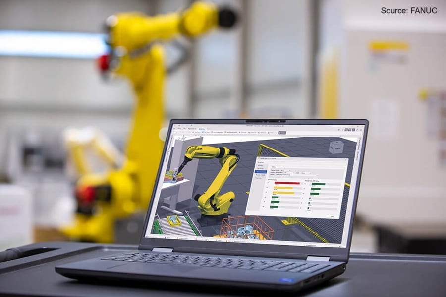 Laptop displaying FANUC robot simulation, with a real robot blurred in background.