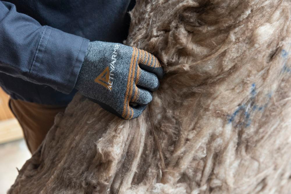 Hand wearing 'ACTIVARMR' glove holding brown insulation.