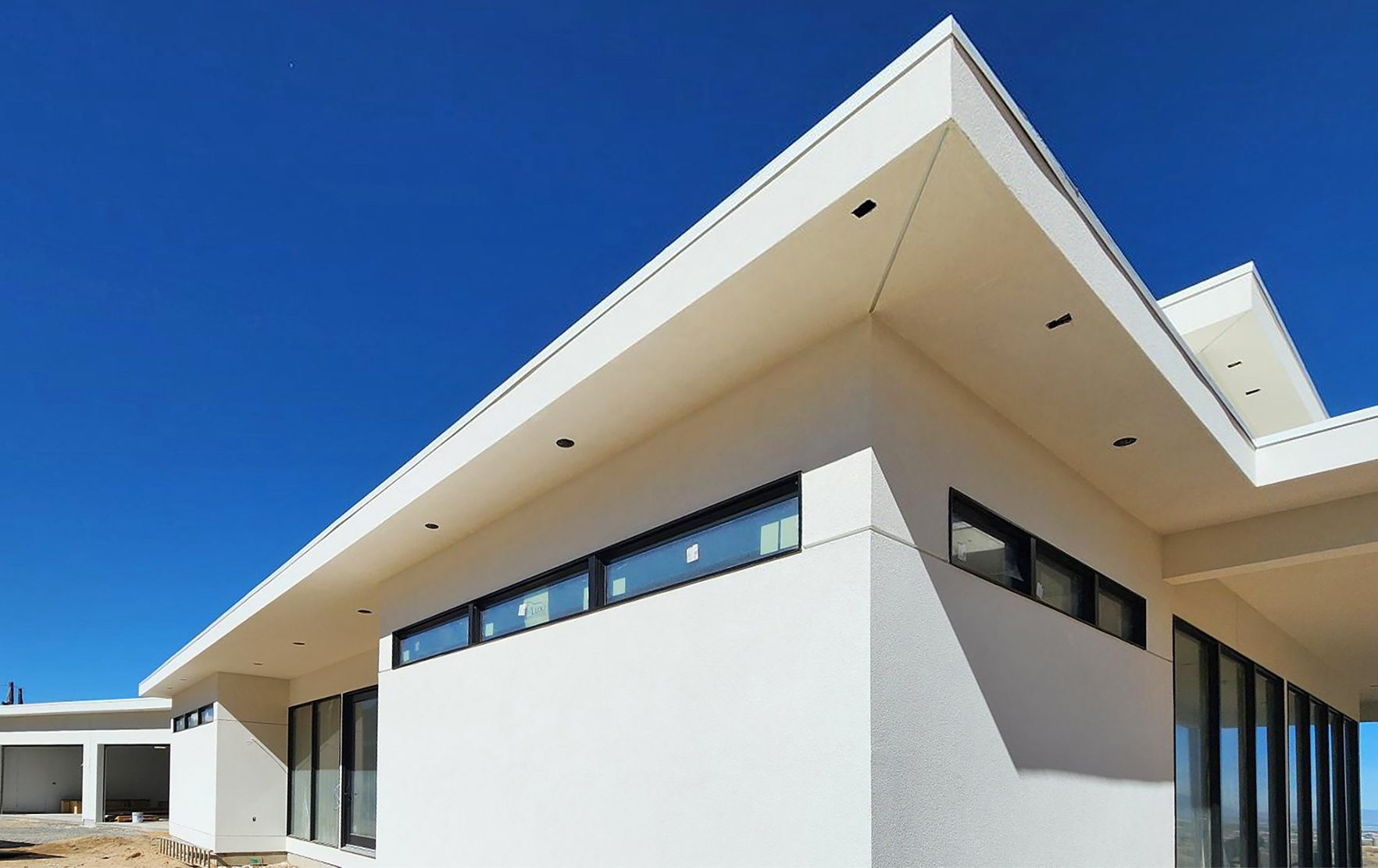 Modern white stucco house with dark-framed windows and a striking roofline against a clear blue sky.