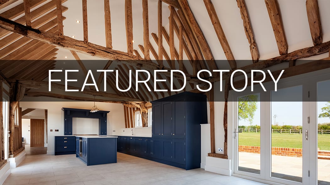 Barn conversion kitchen with exposed beams, navy cabinets, and glass doors to field. Text: 'FEATURED STORY'.