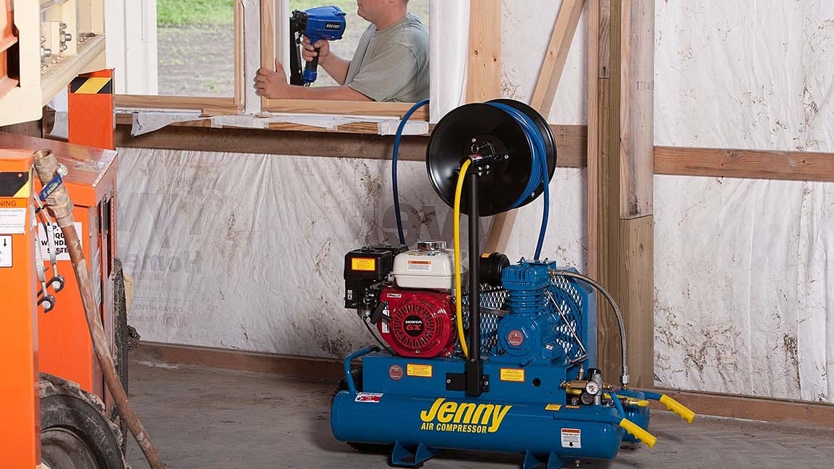 Man using a nail gun on a window, powered by a Jenny air compressor with a hose reel.