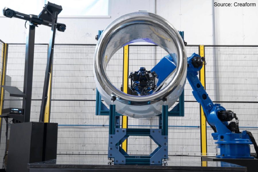 Robotic 3D scanner inspecting a large, shiny cylindrical jet engine part in an industrial setting.