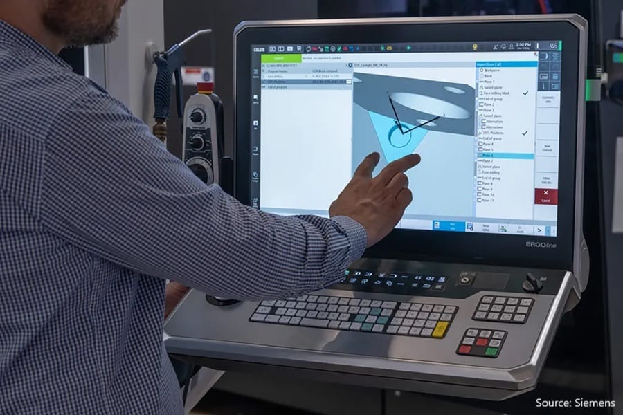 Hand on Siemens ERGOline CNC control screen with CAD model, keyboard visible.