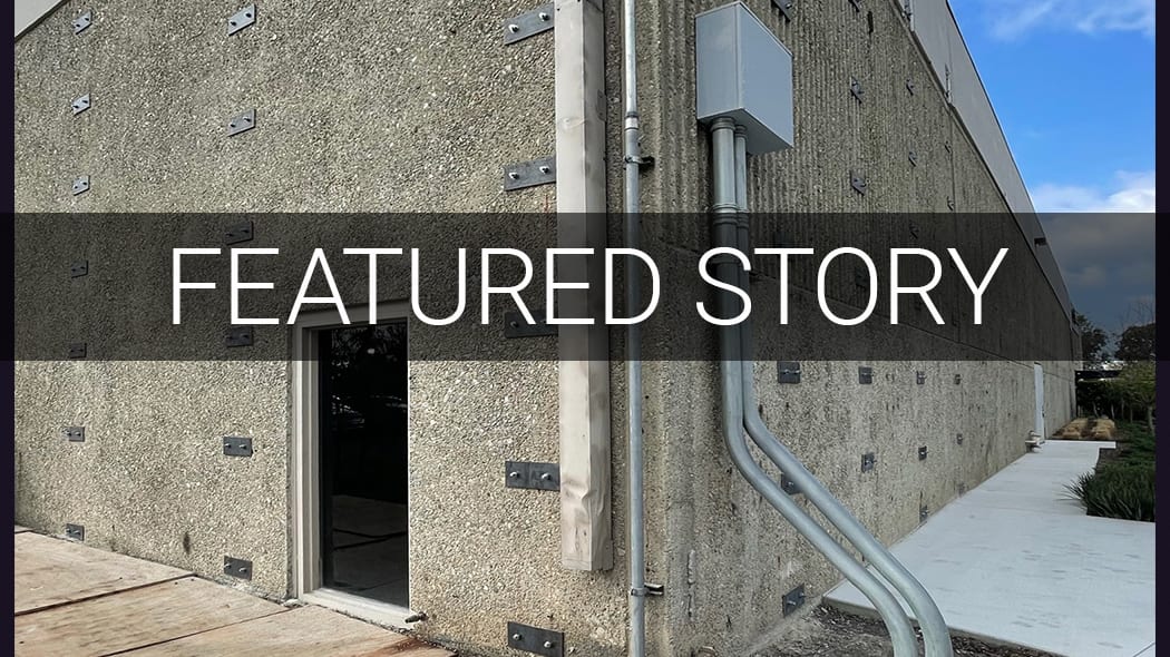 Text "FEATURED STORY" over a concrete building wall with pipes and metal attachments.