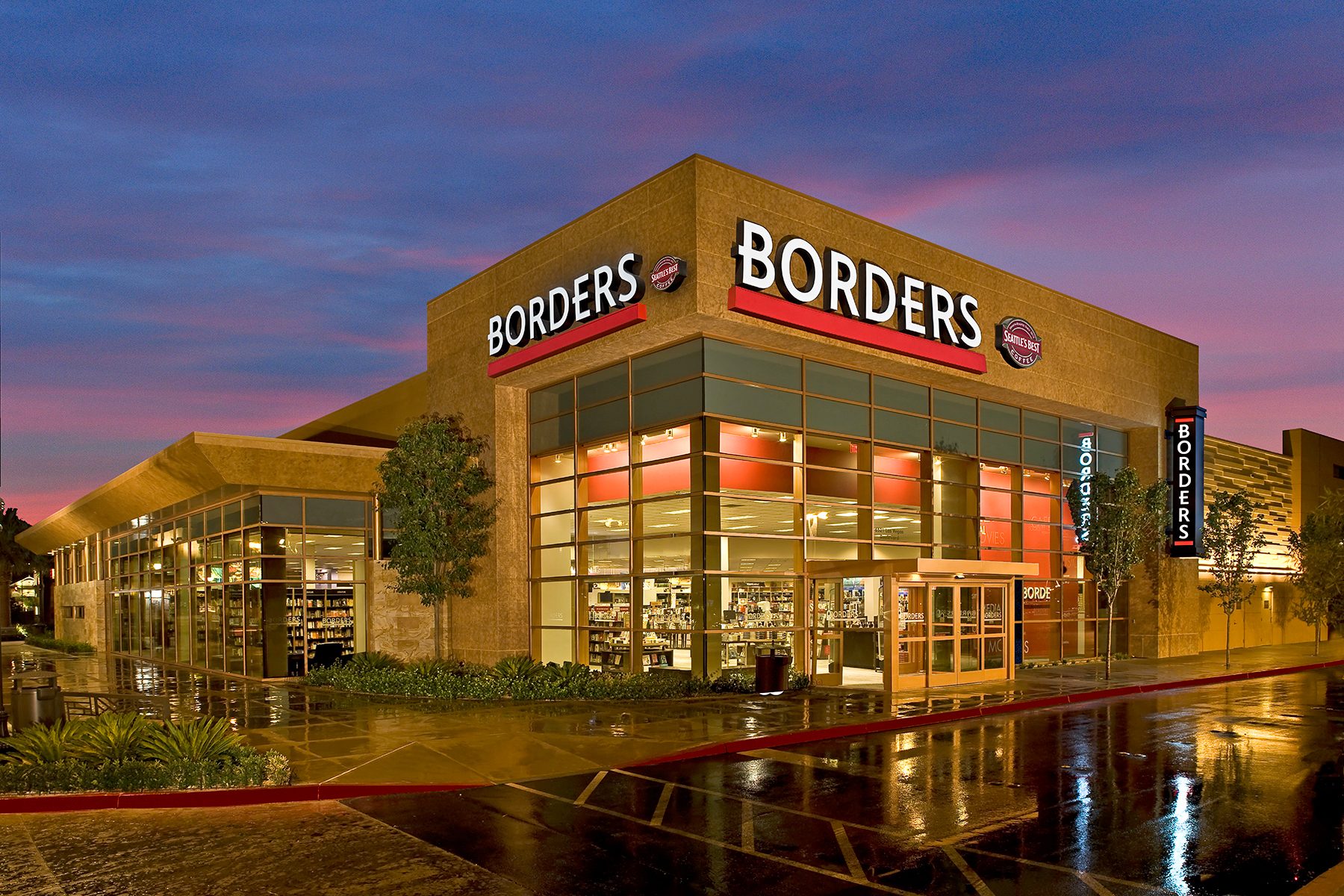 Exterior of a Borders bookstore at dusk, with illuminated signs and wet pavement reflecting lights.