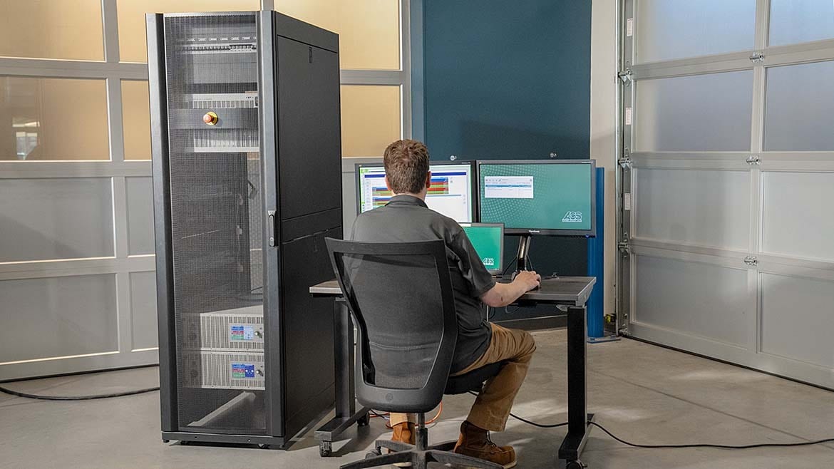 Man works at computers next to a server rack in an industrial setting.
