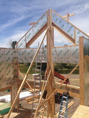 Timber frame structure under construction with reflective insulation and ladders.