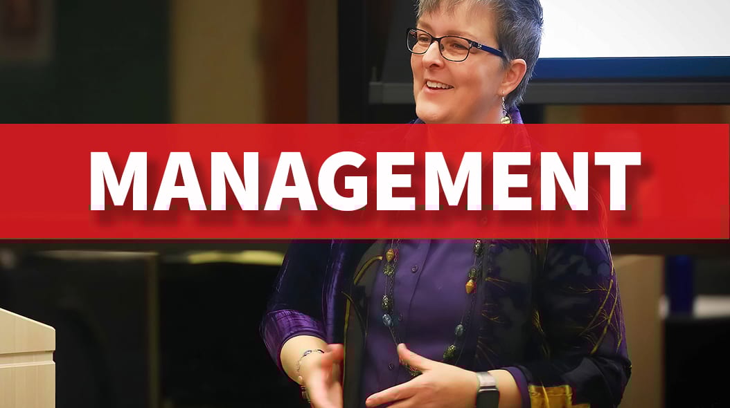 Woman speaking during a presentation, with "MANAGEMENT" text on a red banner overlay.