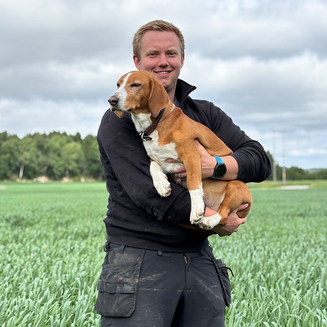 Smiling man holding a brown and white dog in a green field.