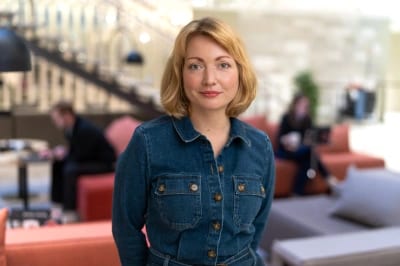 A woman in a denim dress smiles in a modern office lounge.