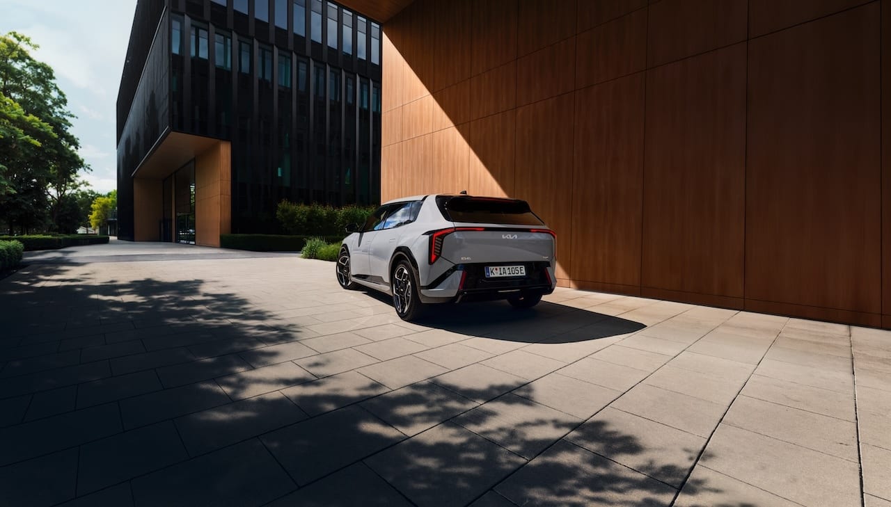 Light gray Kia EV5 parked at a modern building, with tree shadows on the paved ground.