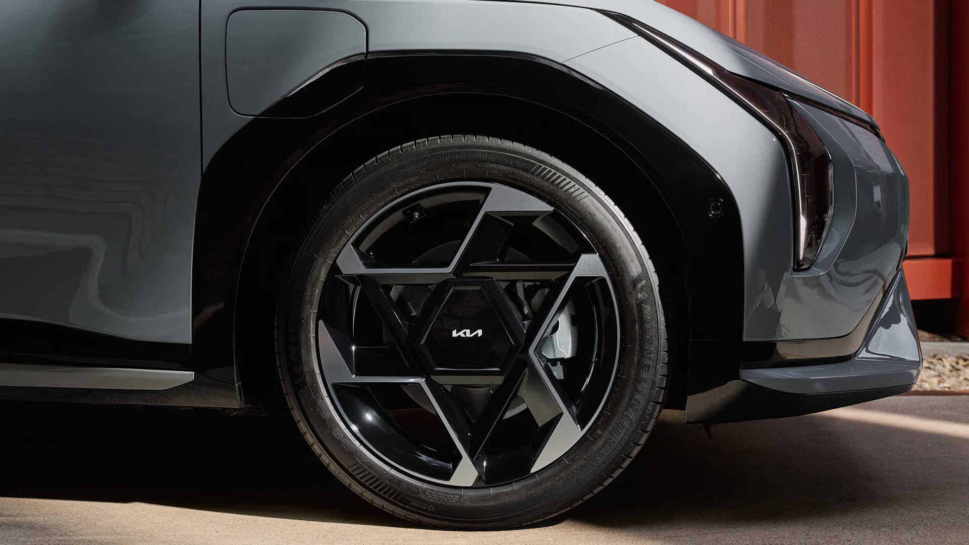 Close-up of a grey car's front wheel with unique geometric Kia-branded rims.