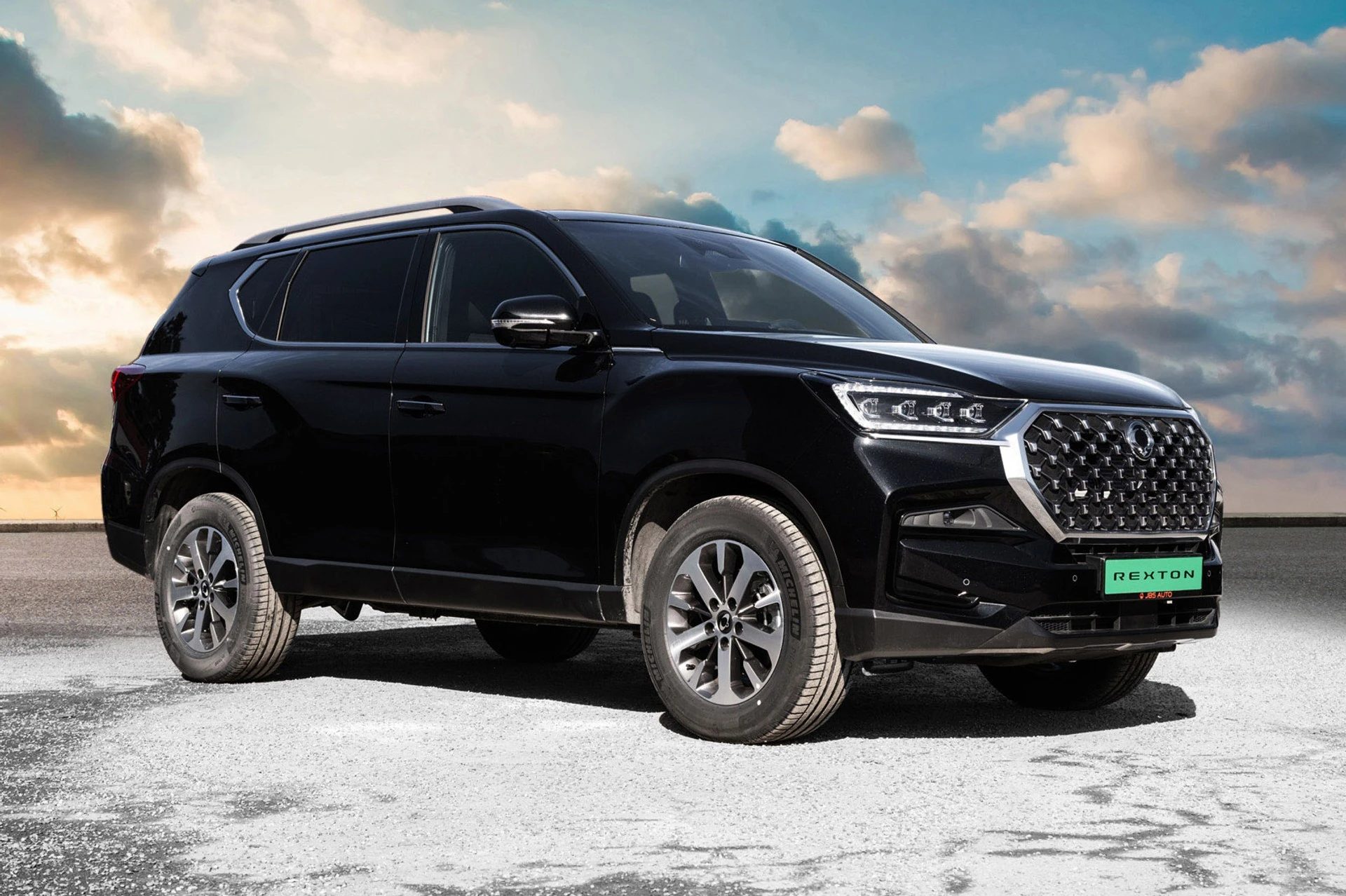 Black SUV (SsangYong Rexton) parked on gravel, under a cloudy sky.