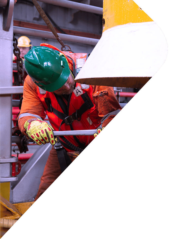 Offshore worker in PPE with hard hat and life vest adjusting equipment with a tool.