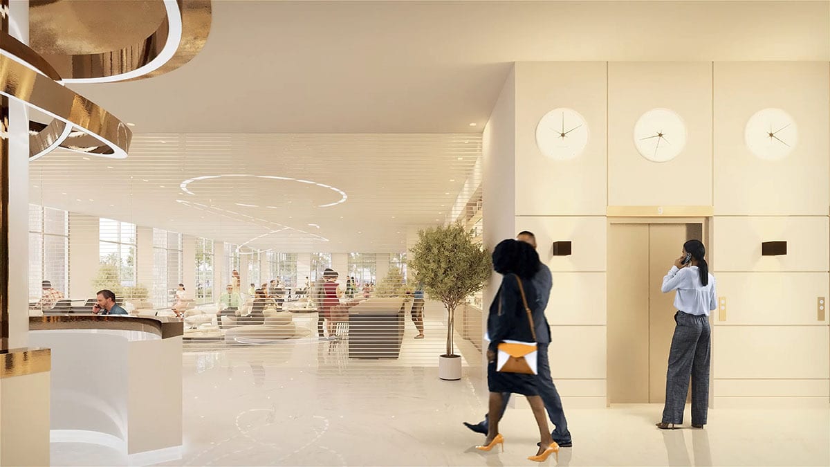 Bright, modern lobby with people, an elevator, and three clocks; a woman is on the phone.