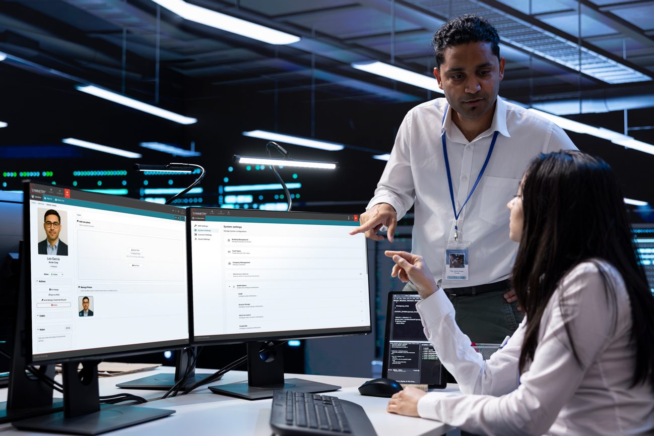 Two IT professionals collaborate in a server room, pointing at system settings on a computer screen.