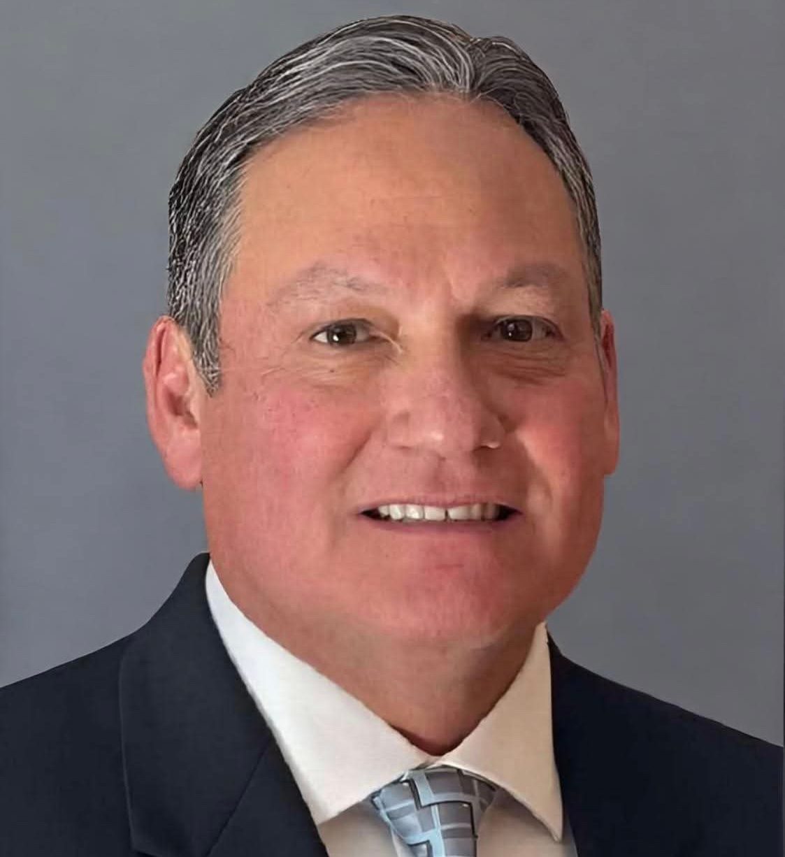 Smiling man with gray hair, dark suit, and patterned tie.