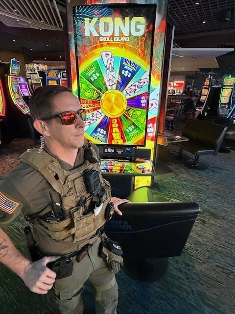 Man in tactical vest and sunglasses by a Kong slot machine in a casino.