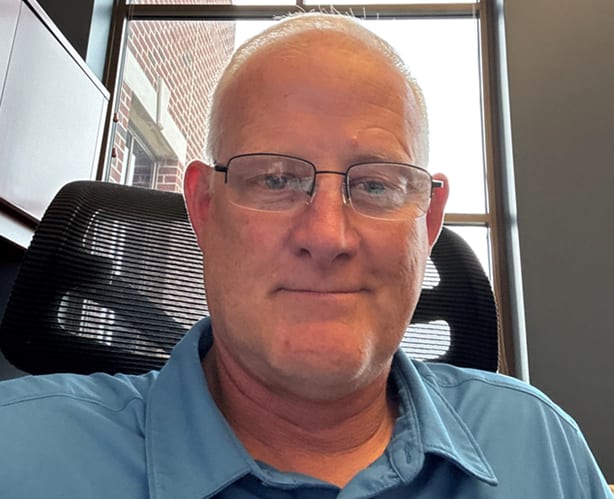 Smiling man with glasses and blue shirt in an office.