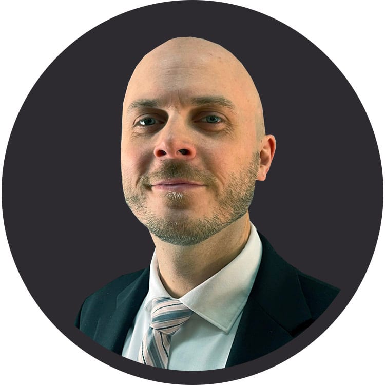 Smiling bald man with a beard, wearing a suit and striped tie in a circular frame.