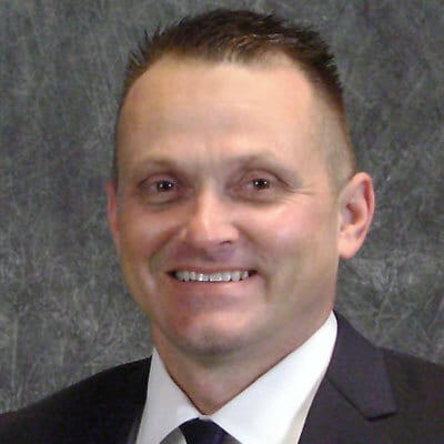 Smiling man with short dark hair in a suit and tie.