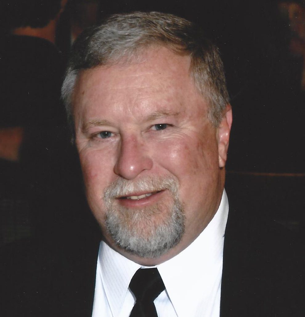 Headshot of a smiling man with graying hair and a goatee, wearing a suit.