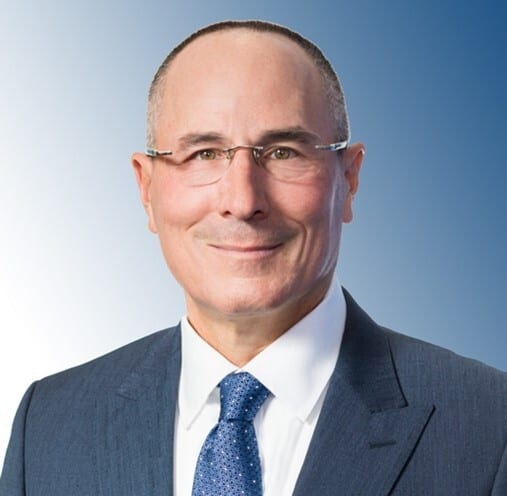 Smiling man in a suit and glasses against a blue background.