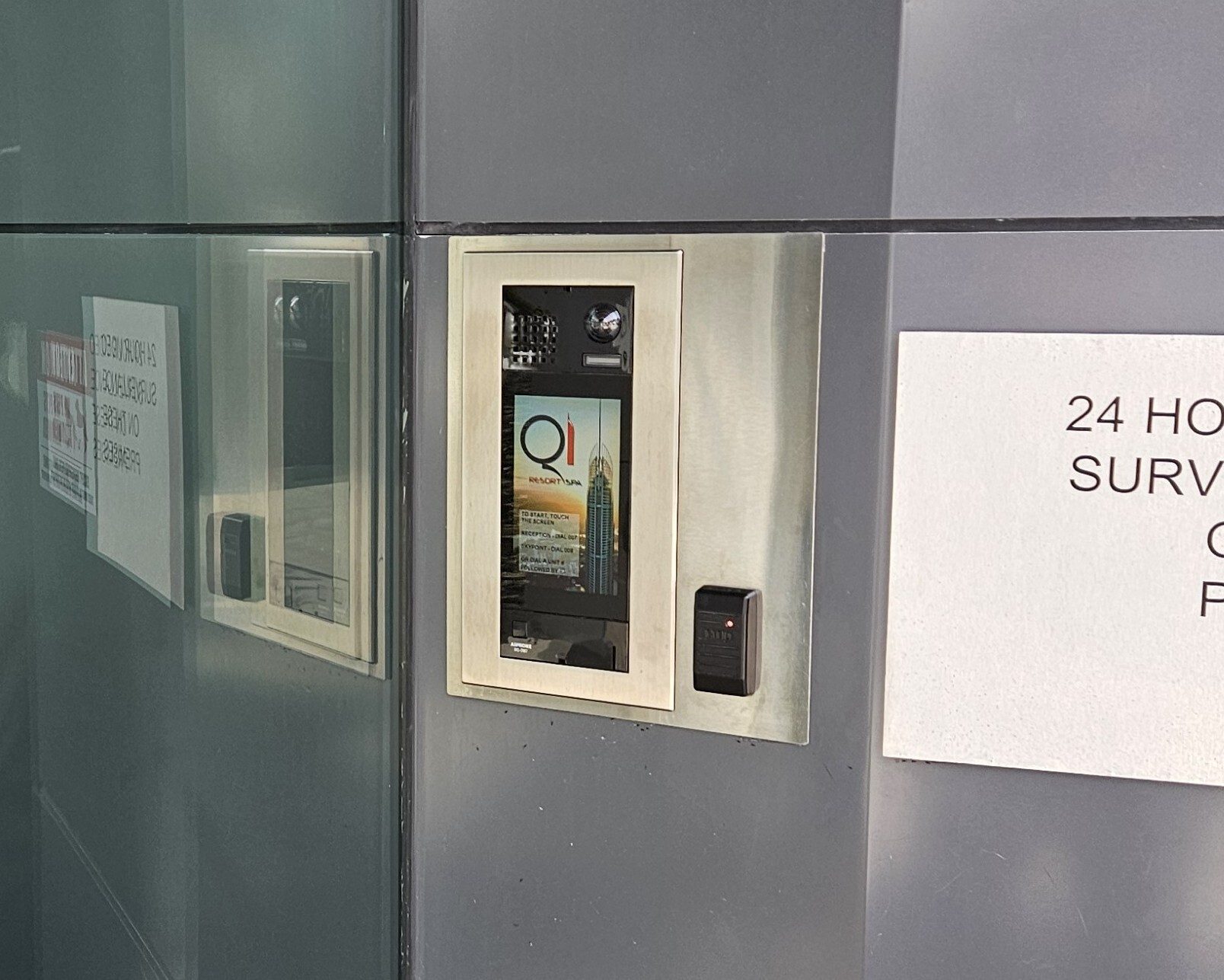 Building entry system with digital screen showing 'Q1 Resort Spa', card reader, and warning signs.