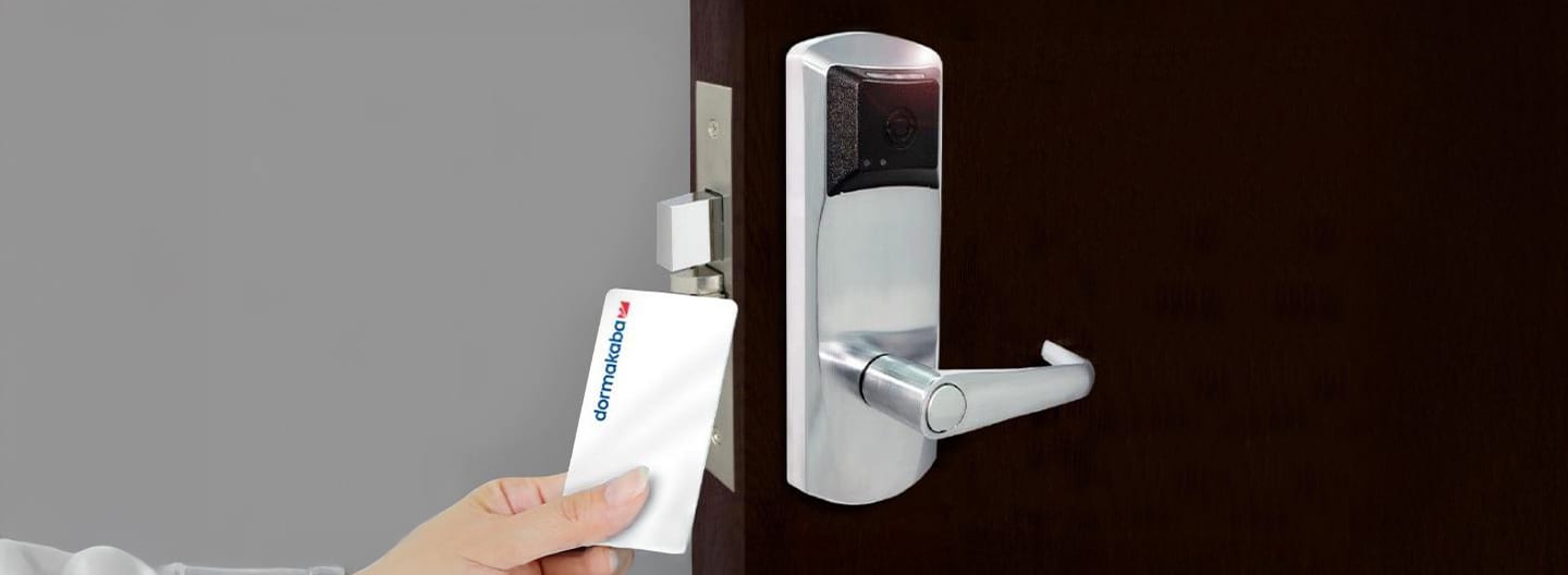Hand inserting "dormakaba" key card into an electronic door lock, showcasing modern access control.