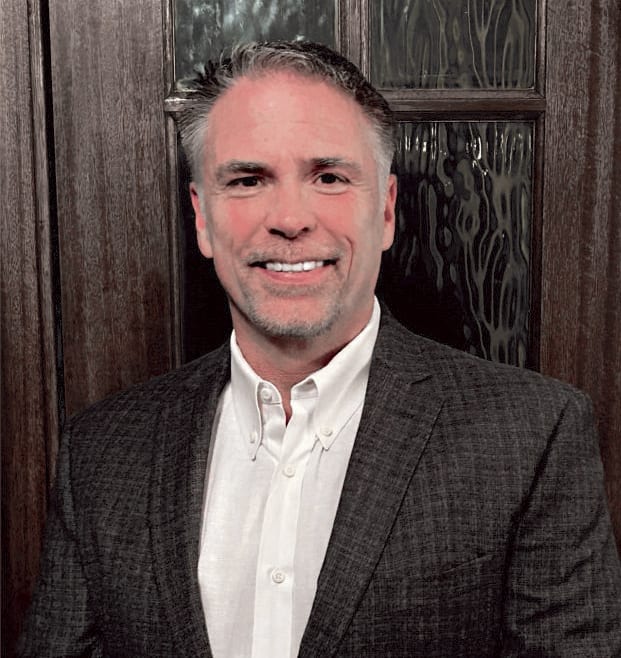 Smiling man in a dark suit and white button-down shirt.