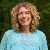 Smiling woman with curly hair wearing a light blue top.