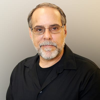 A middle-aged man with glasses and a gray beard, wearing a black shirt, looking at the camera.