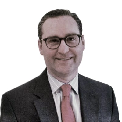 Smiling man in glasses, dark suit, and pink tie.