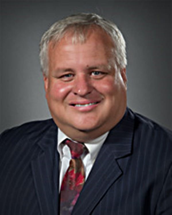Smiling man with gray hair, wearing a pinstripe suit and patterned tie.