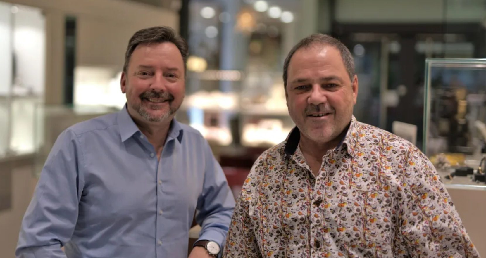 Two smiling men standing side-by-side indoors.