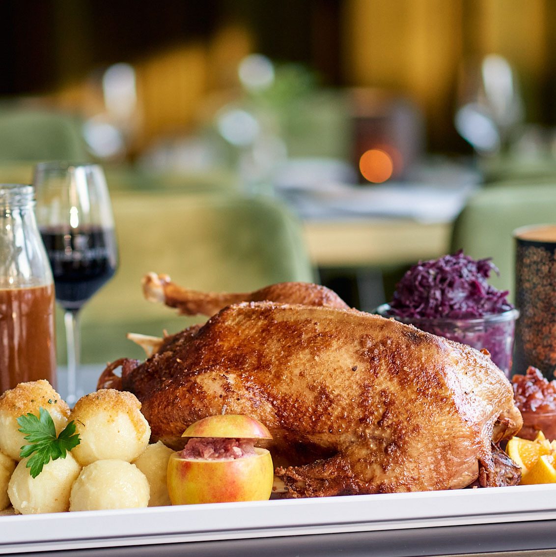 Roasted duck with potato dumplings, red cabbage, and a stuffed apple on a white platter.