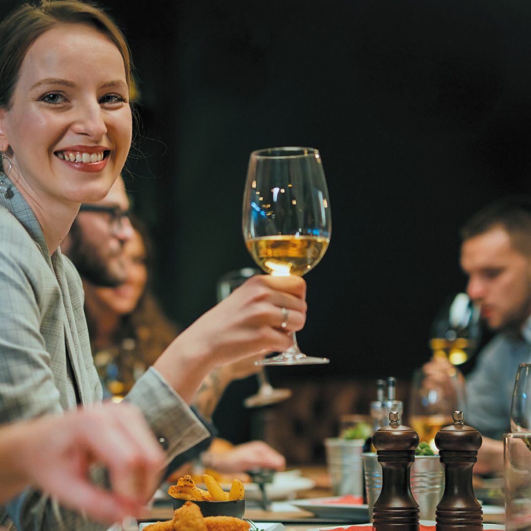 Smiling woman holding white wine glass at dinner.