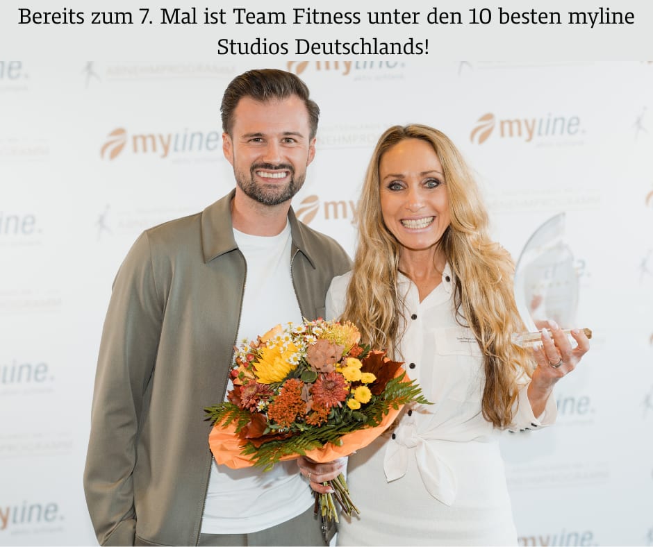 Smiling man and woman with flowers and an award, celebrating Team Fitness's repeated top ranking.