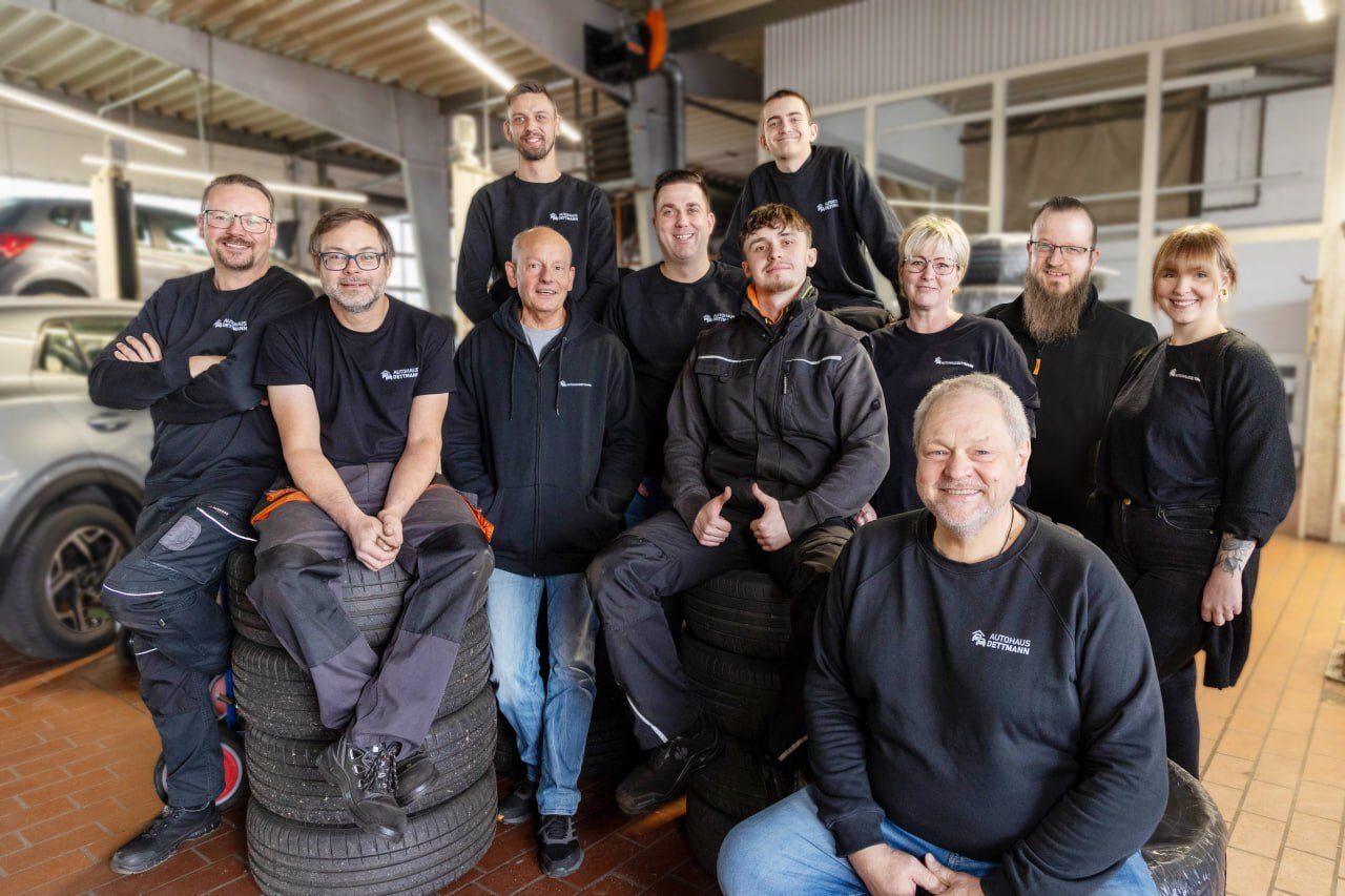Smiling team from Autohaus Dettmann in their auto shop, some sitting on tires.